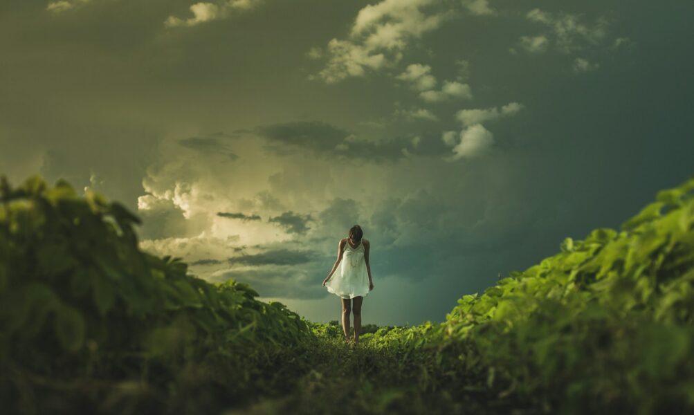 woman wearing white dress standing on hill with green grass under white cloudy sky