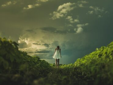 woman wearing white dress standing on hill with green grass under white cloudy sky