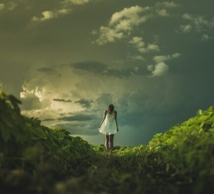 woman wearing white dress standing on hill with green grass under white cloudy sky